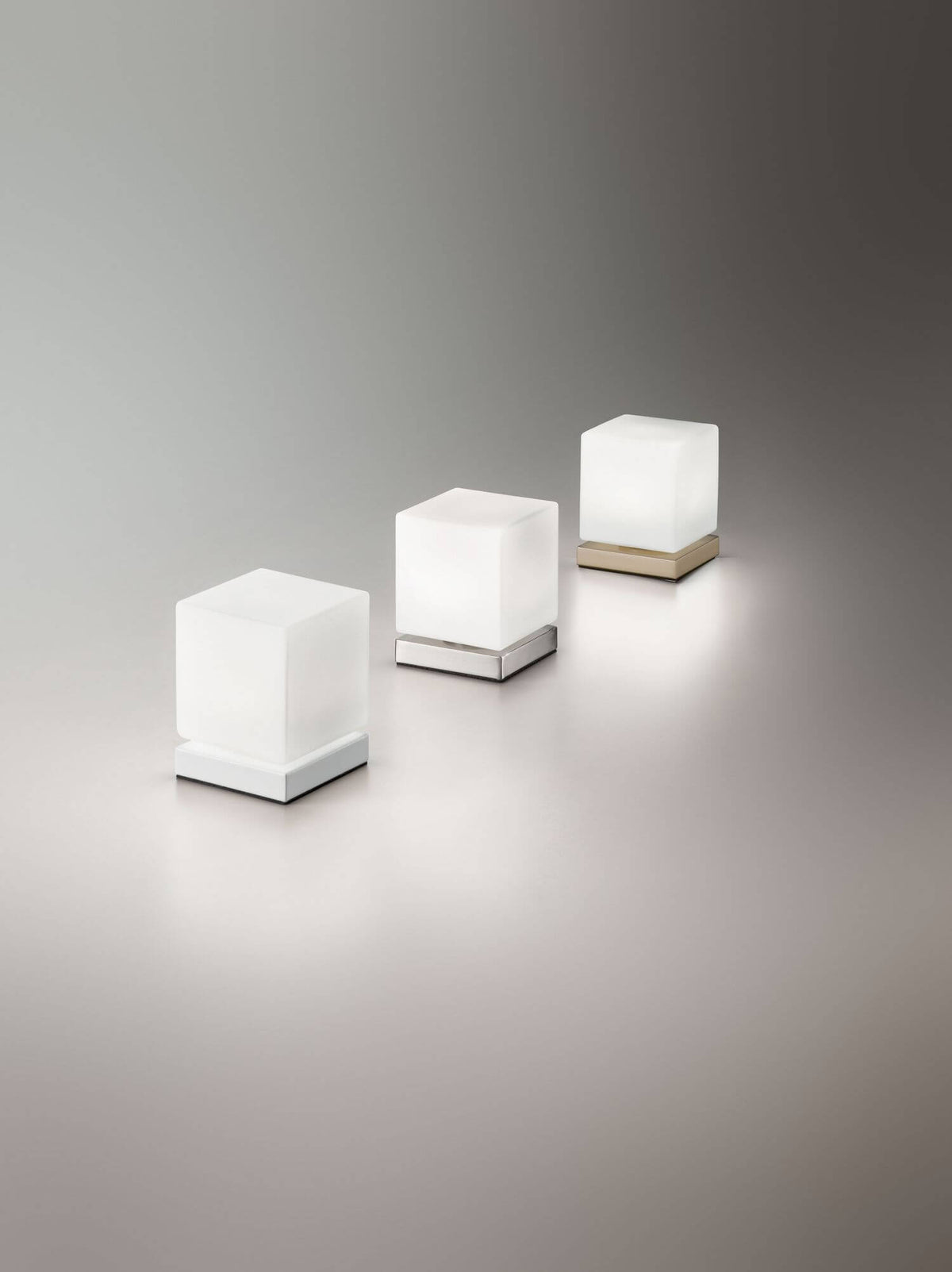 Trois déclinaisons du cube lumineux aux socles blanc, chrome et laiton