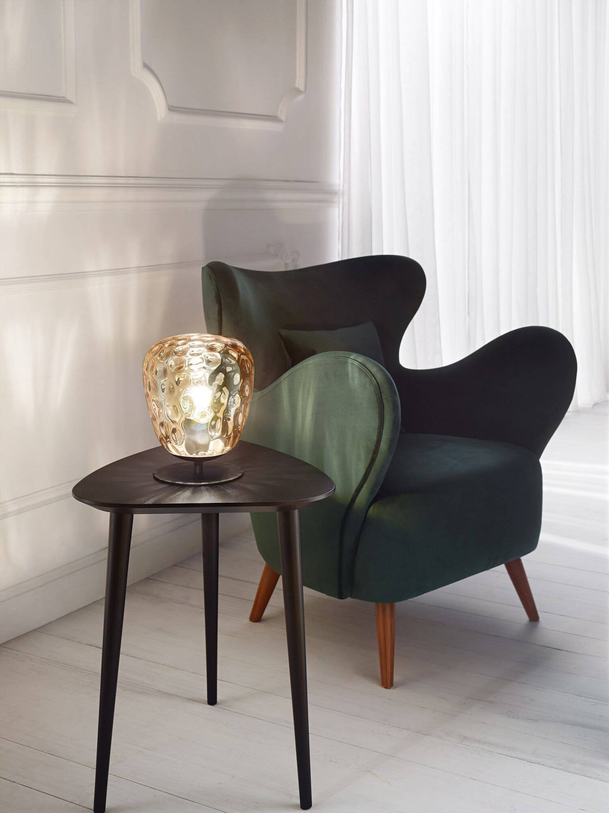 Mise en ambiance, lampe allumée sur table basse devant fauteuil vert