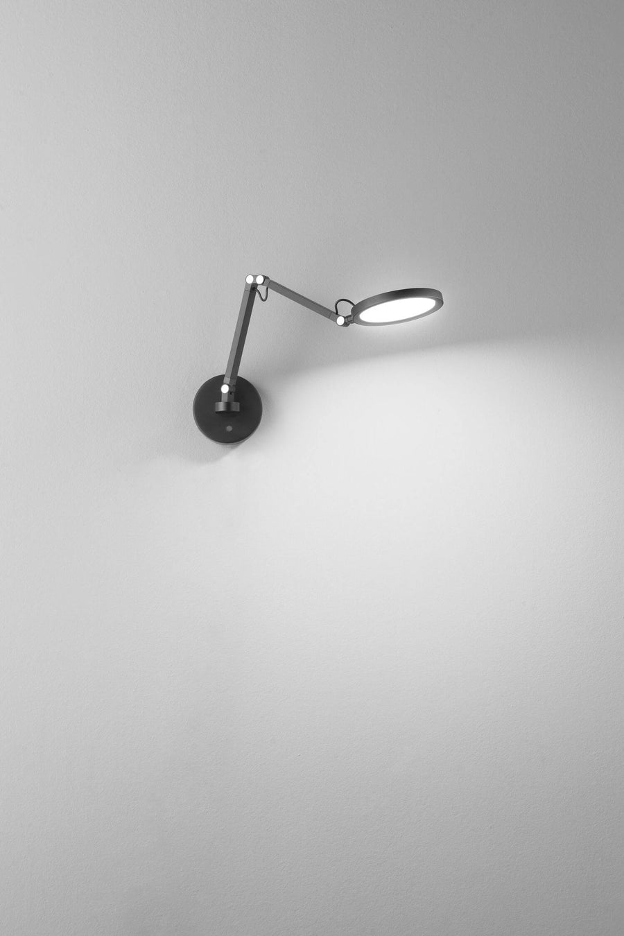 Applique noire fixée au mur, diffusant une lumière blanche sur la surface claire
