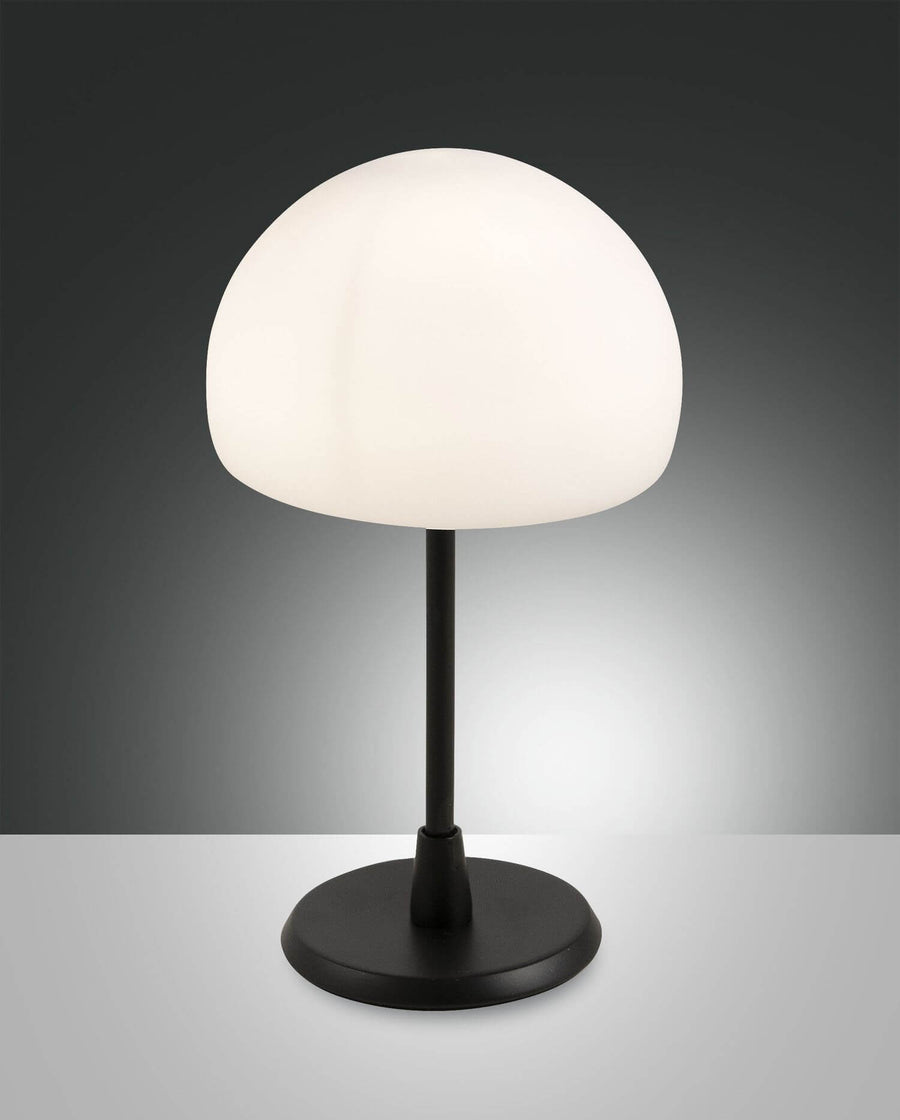 Lampe à poser noire de face sur fond gris, abat-jour opalin blanc allumé