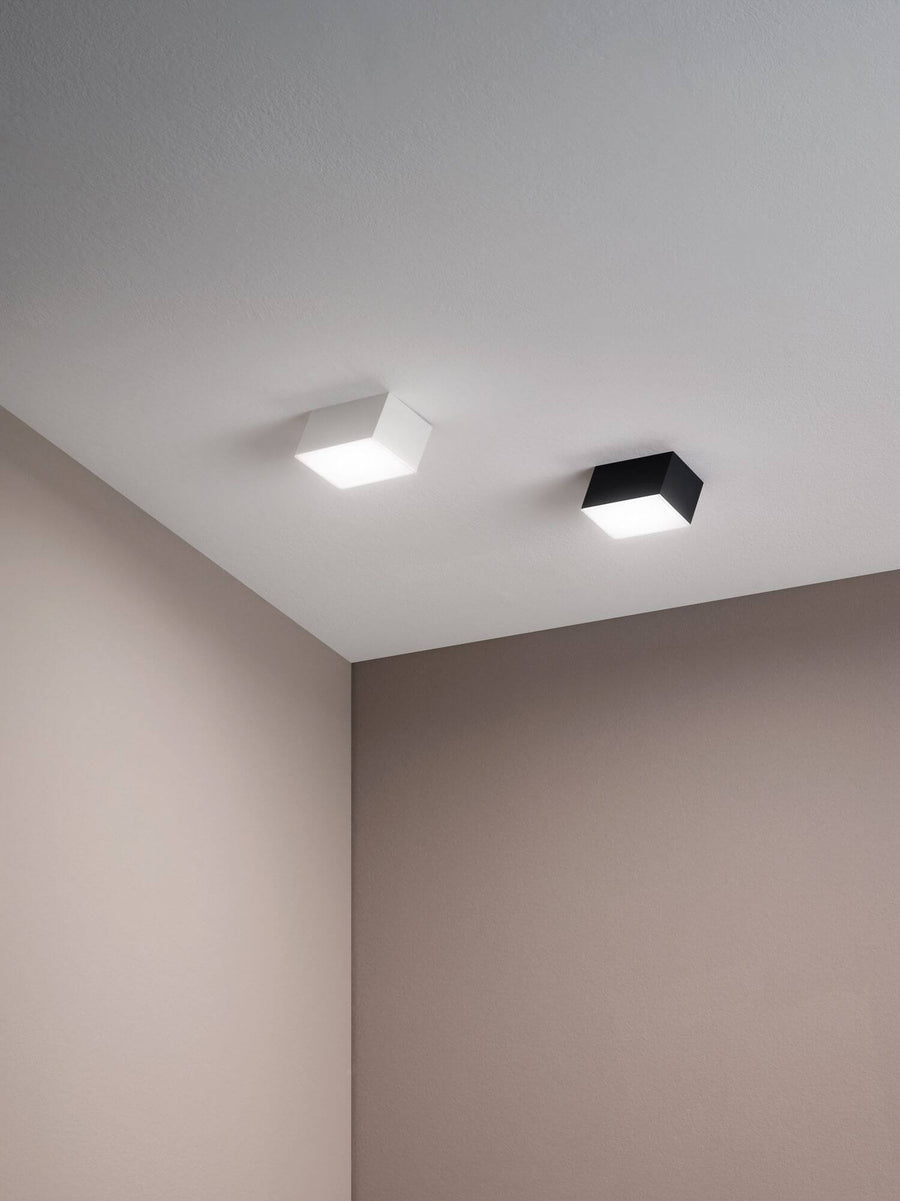Deux spots carrés fixés au plafond dans un coin de pièce, un blanc et un noir