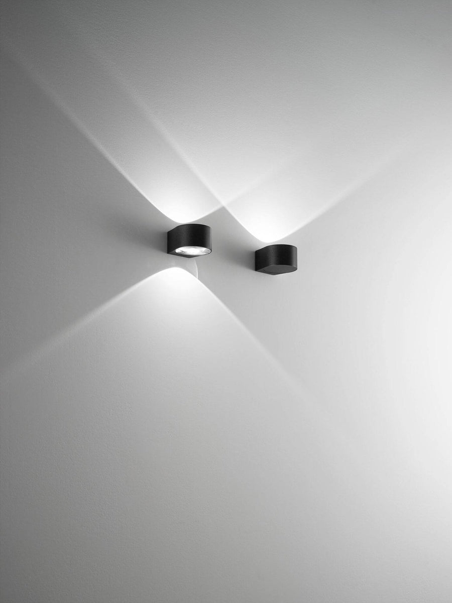 Deux appliques noires fixées au mur, faisceaux lumineux croisés vers le haut