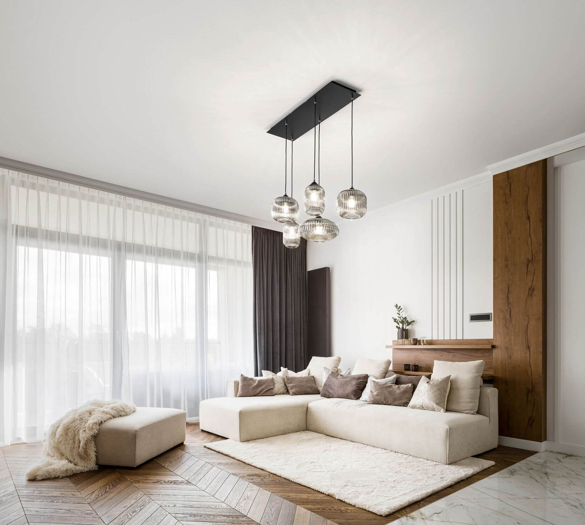 Suspension installée au plafond dans un salon moderne, canapé beige et grandes fenêtres
