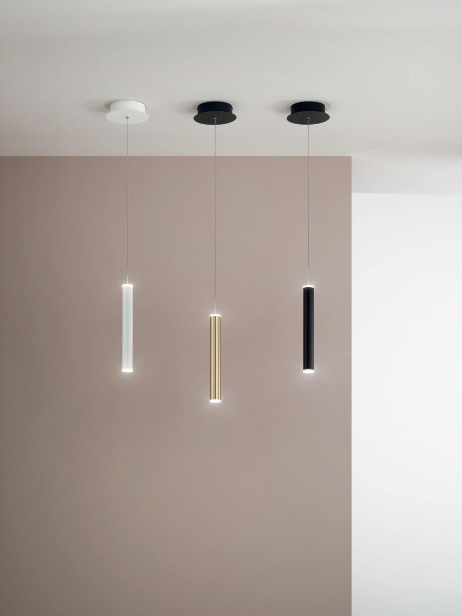 Trois suspensions cylindriques blanche, dorée et noire fixées au plafond devant un mur beige