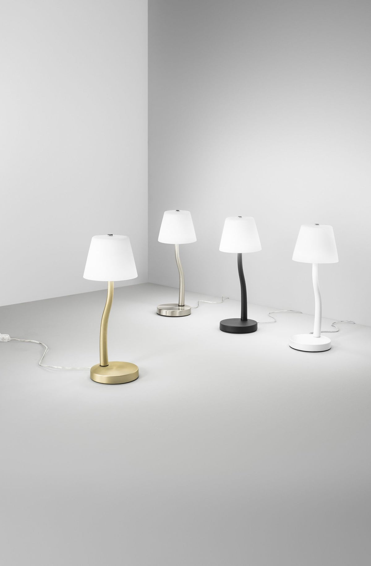 Quatre lampes identiques en finitions dorée, acier, noire et blanche dans une pièce grise