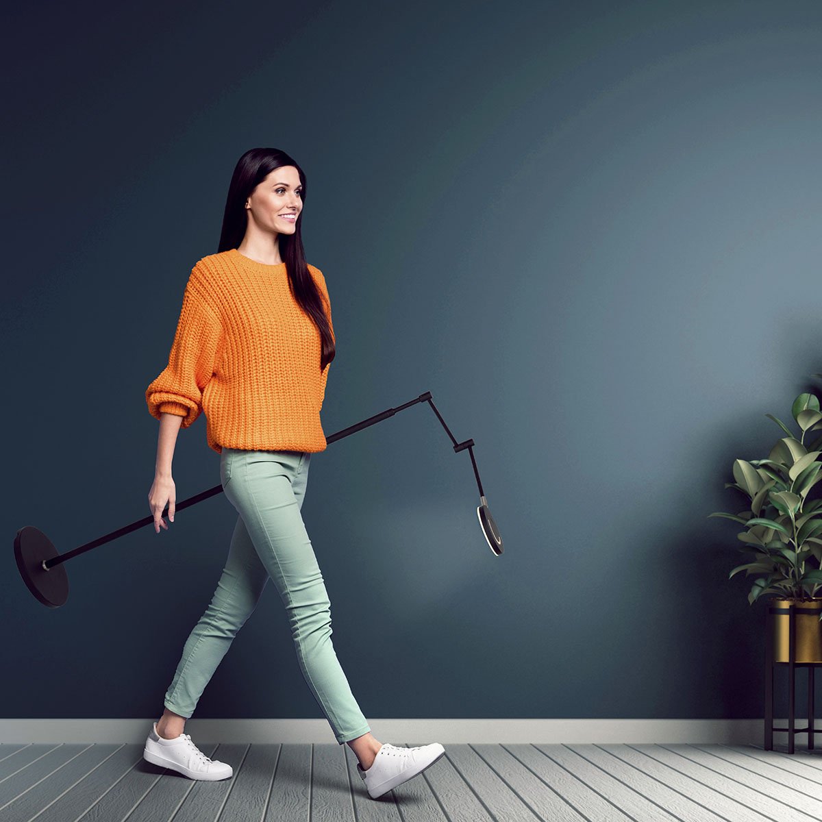 Femme portant le lampadaire plié et incliné devant un mur gris-bleu