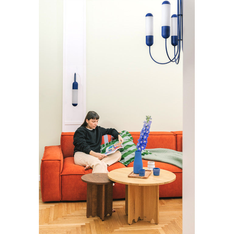 Mise en ambiance salon avec lustre bleu suspendu, femme lisant sur canapé orange