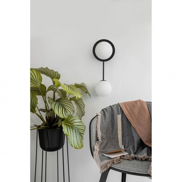 Mise en ambiance murale blanche avec plante verte, fauteuil et plaid.