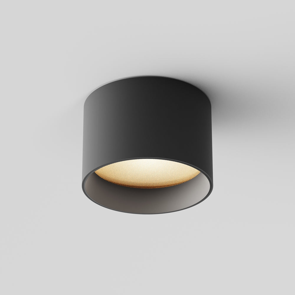 Vue en contre-plongée du plafonnier cylindrique noir, réflecteur doré et diffuseur rétroéclairé.