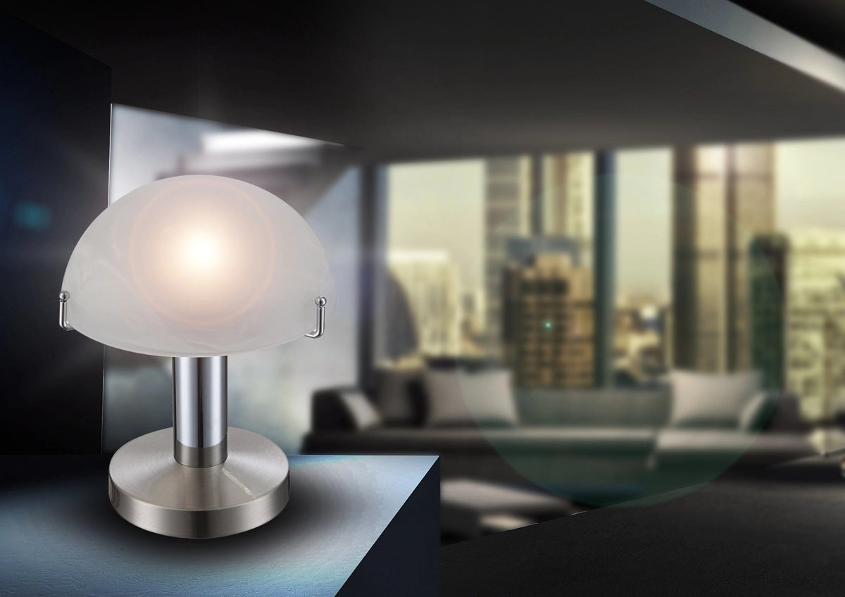 Mise en ambiance : lampe allumée posée sur un meuble, intérieur contemporain et vue urbaine floue.