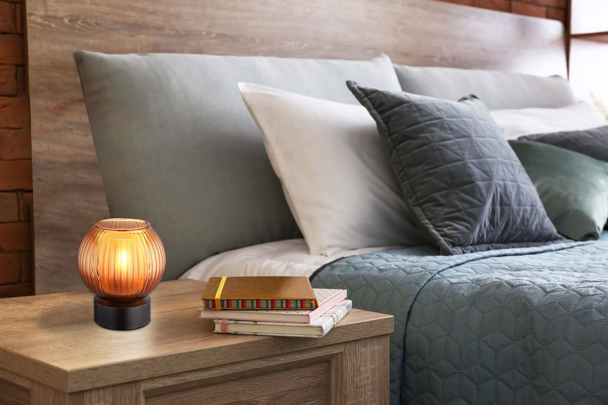 Mise en ambiance : lampe allumée sur une table de chevet en bois, près d'un lit