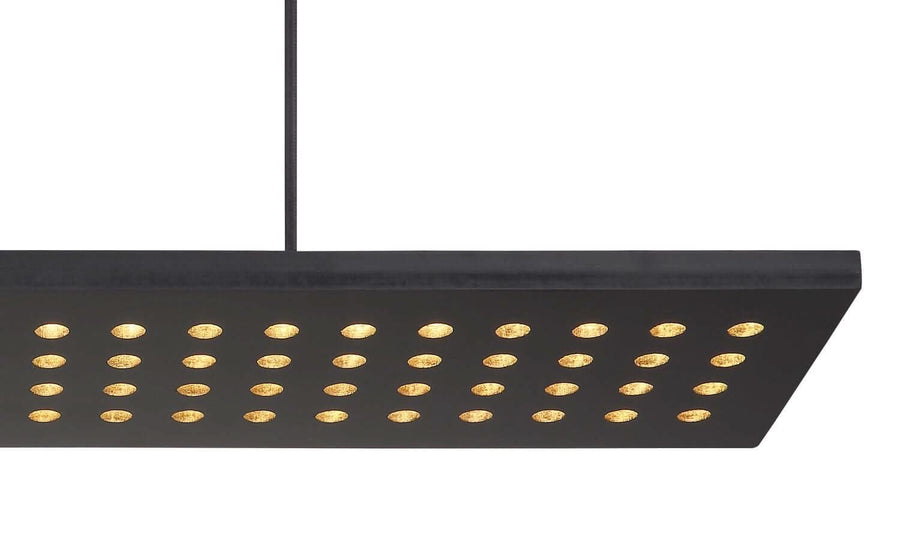 Détail rapproché du diffuseur noir ajouré, montrant les perforations dorées alignées en rangs réguliers.
