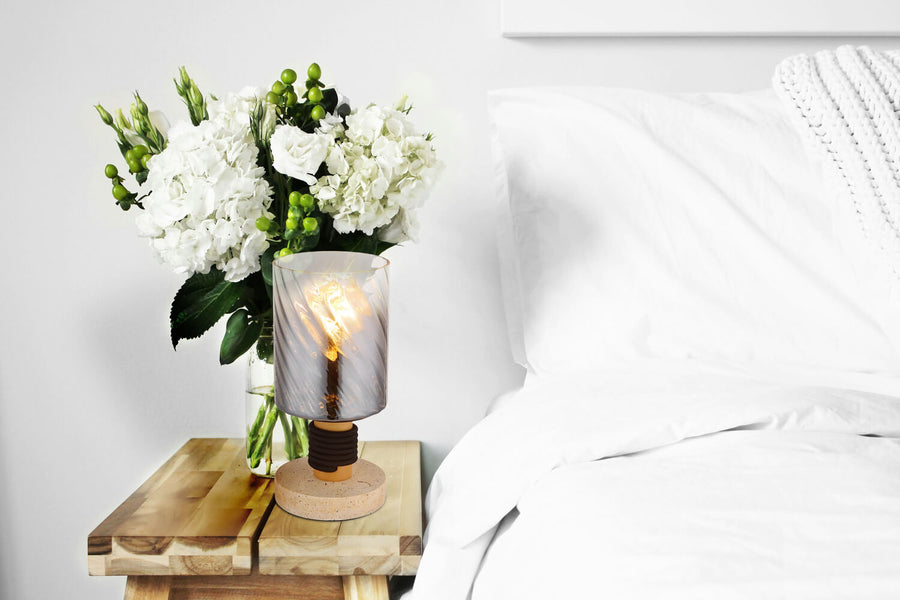 Lampe posée sur une table de chevet en bois, près d'un bouquet de fleurs blanches.