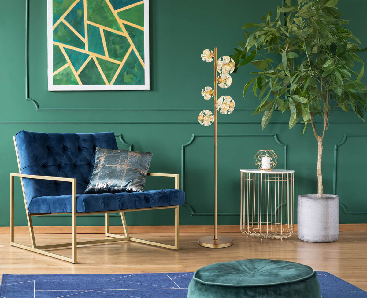 Mise en ambiance du lampadaire doré dans un salon vert, près d'un fauteuil bleu.