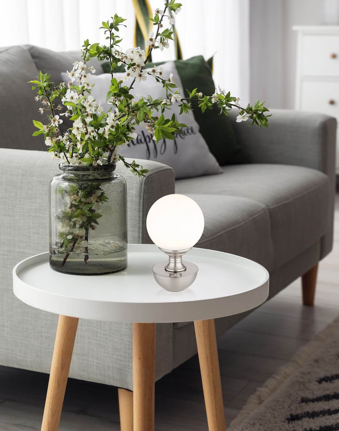 Mise en ambiance sur table d'appoint près d'un canapé et d'un vase fleuri.