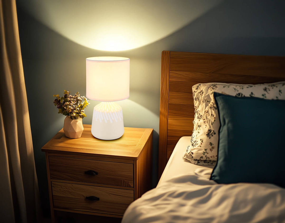 Mise en ambiance : lampe allumée sur table de chevet en bois, chambre