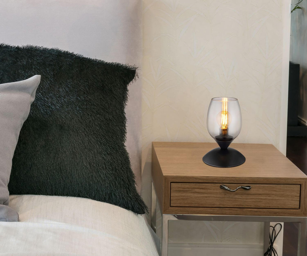 Mise en ambiance, lampe allumée posée sur une table de chevet en bois
