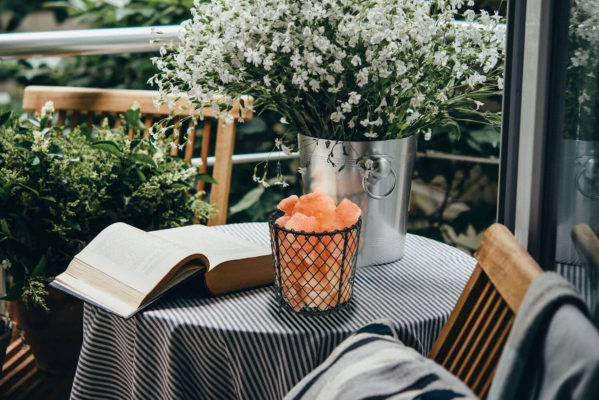Lampe à poser sur table avec livre ouvert, fleurs et vue de balcon.