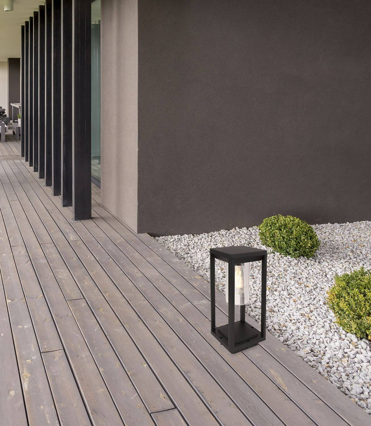 Mise en ambiance sur terrasse en bois, luminaire posé près de graviers.