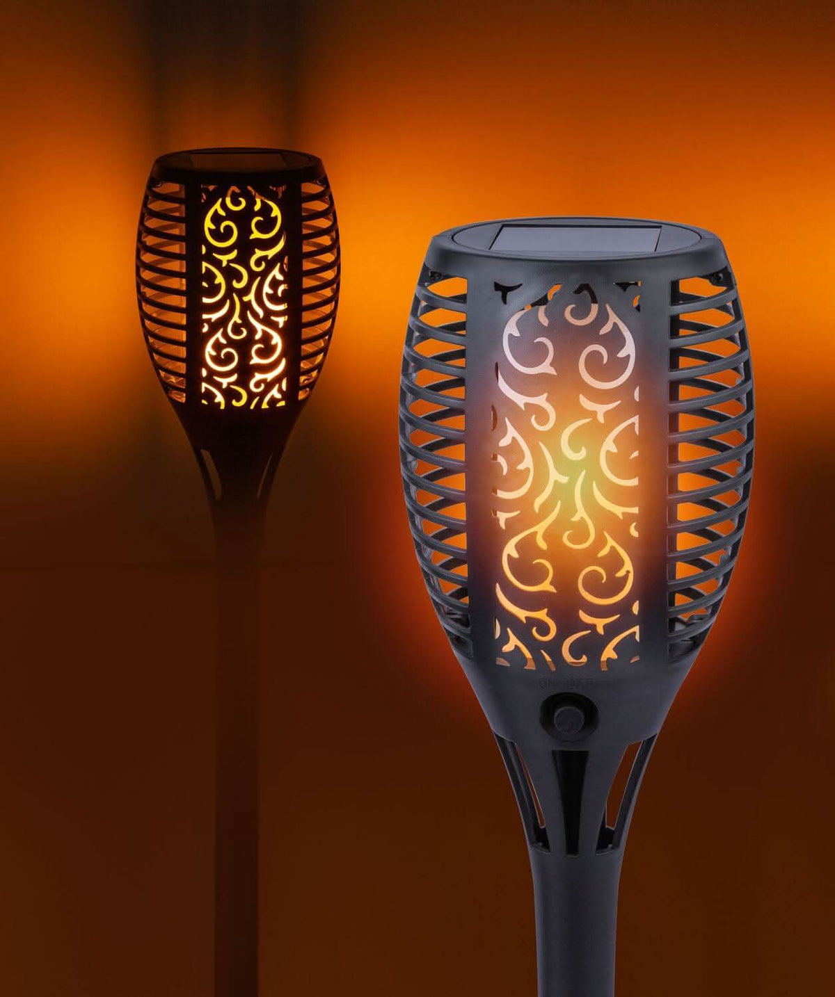 Deux luminaires torches allumés dans une ambiance orange, effet flamme et motif découpé.