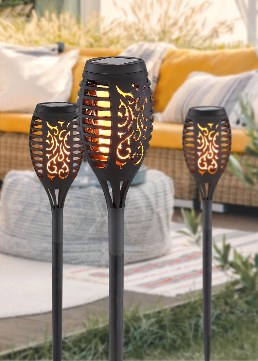 Trois lampes torches solaires noires lumineuses dans un décor extérieur chaleureux.