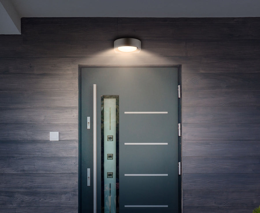 Luminaire mural installé au-dessus d'une porte, éclairant la façade en bois foncé.