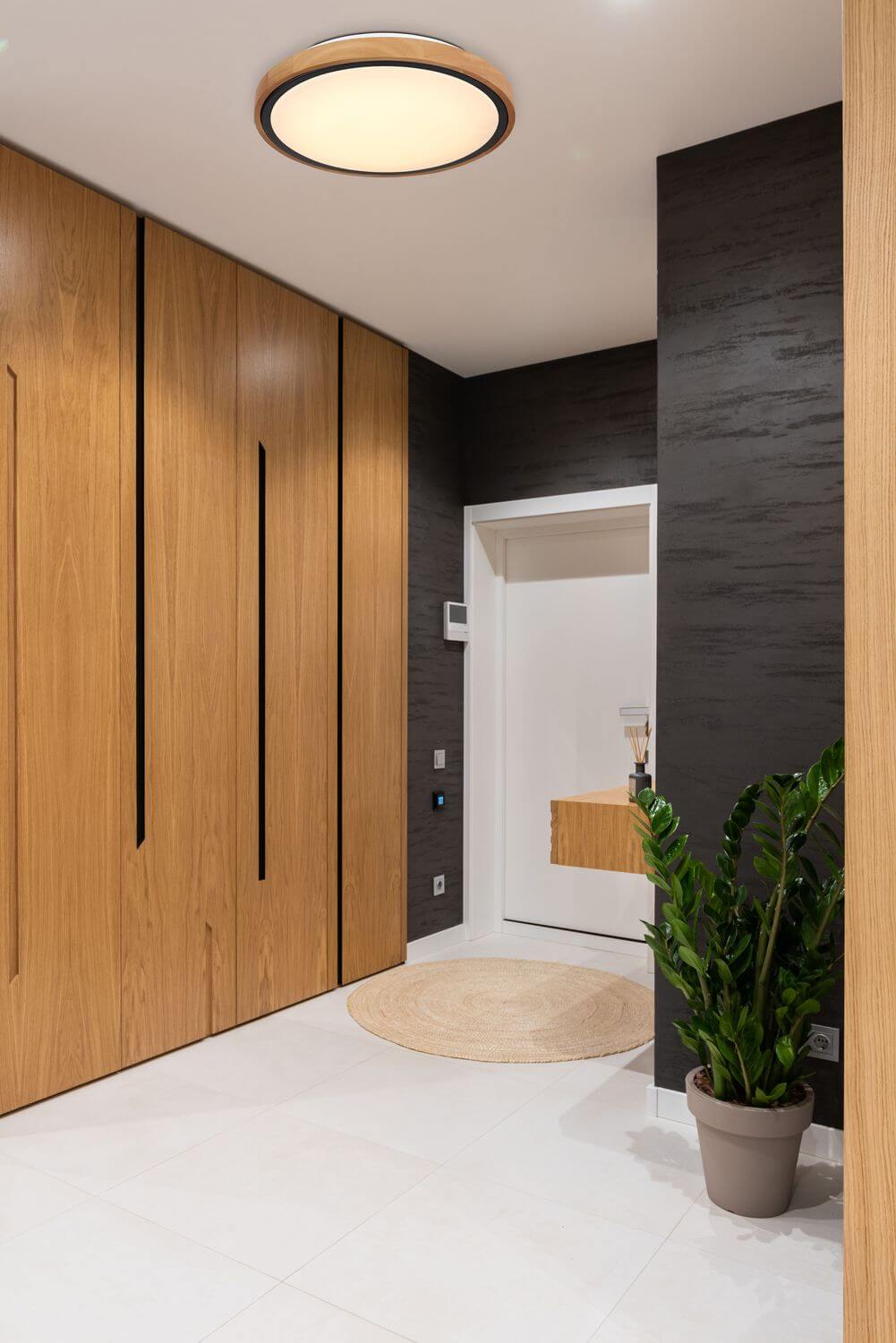Mise en ambiance dans une entrée moderne, plafonnier allumé au-dessus du sol clair