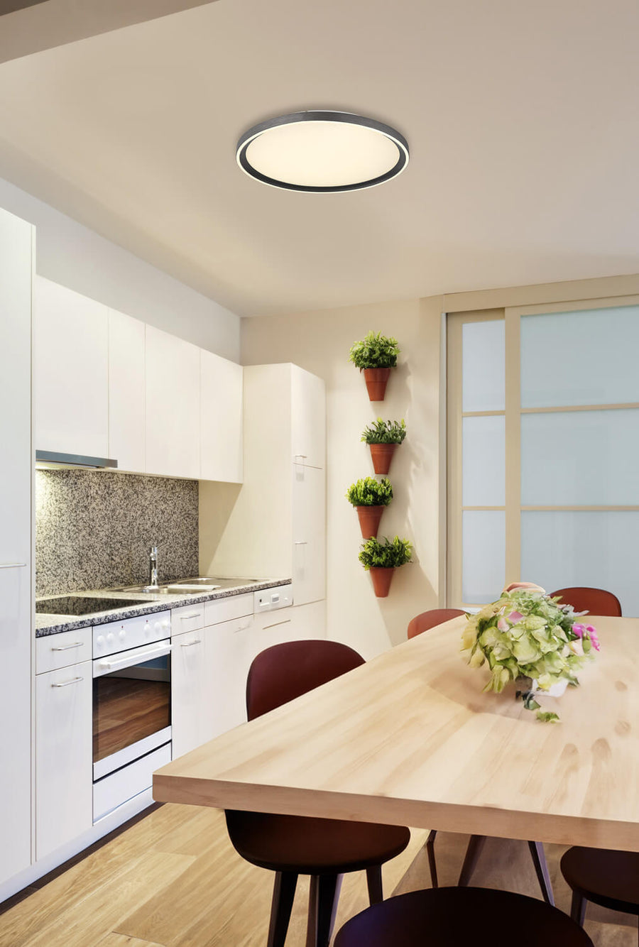 Plafonnier allumé au plafond d'une cuisine blanche avec table en bois clair