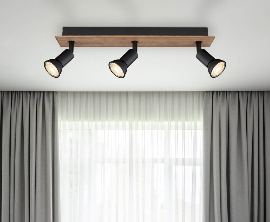 Mise en situation du spot plafond au-dessus d'une fenêtre avec rideaux gris et voilages blancs.