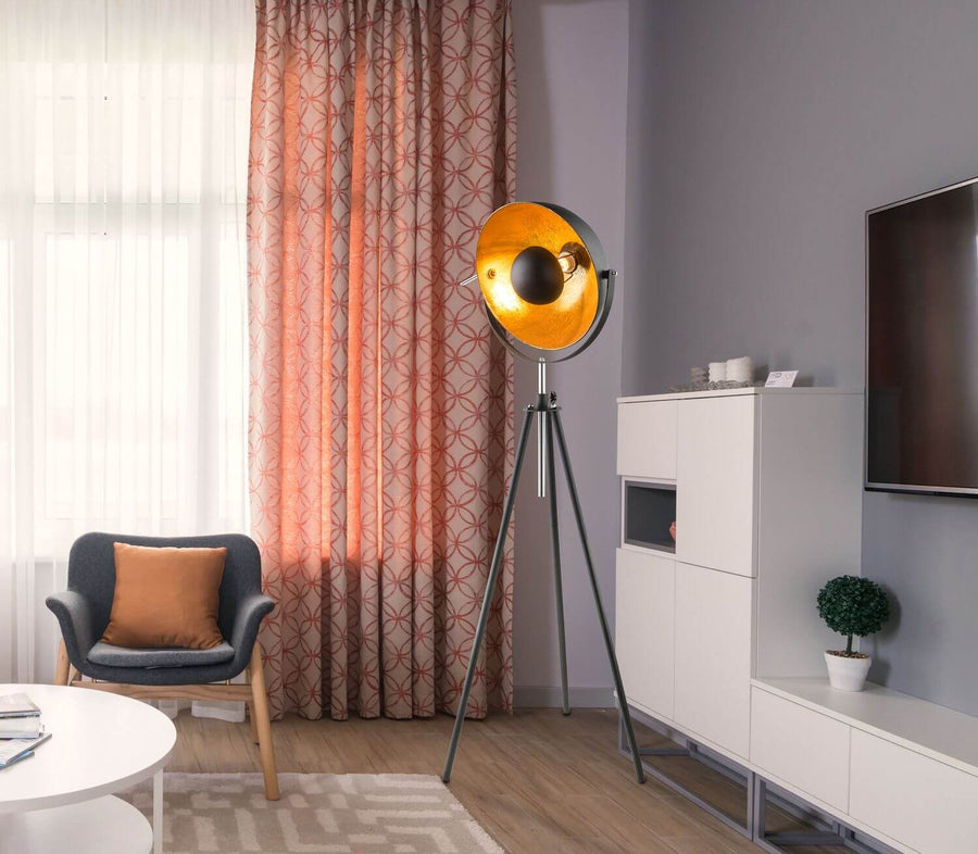 Mise en scène du lampadaire trépied dans un salon moderne avec fauteuil et rideaux.
