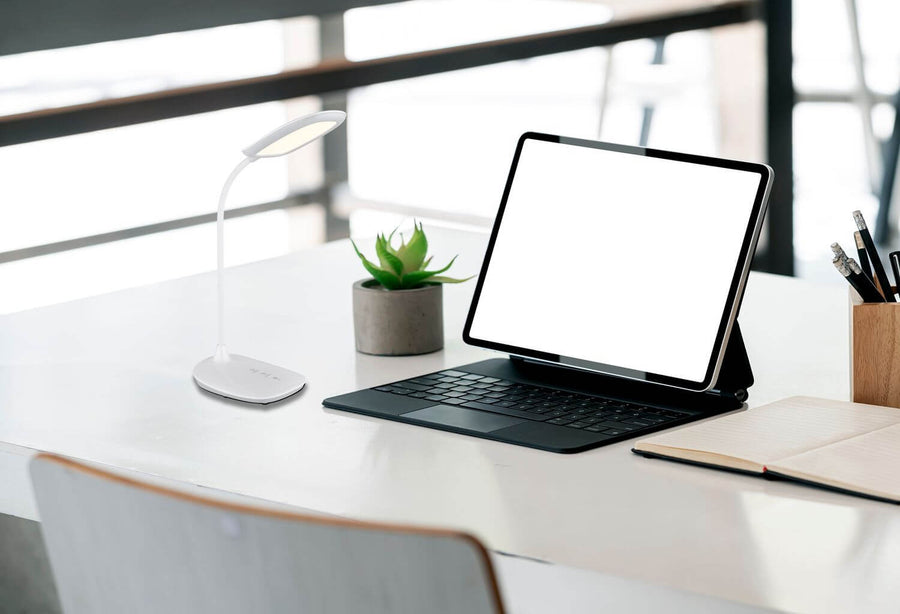 Lampe posée sur un bureau près d'un ordinateur et d'une plante.