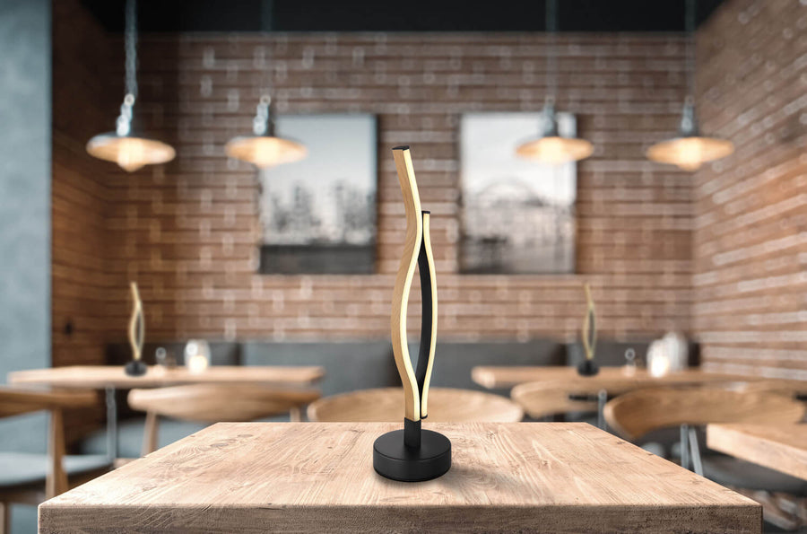Lampe à poser sur table en bois dans un café, arrière-plan flou et chaleureux.