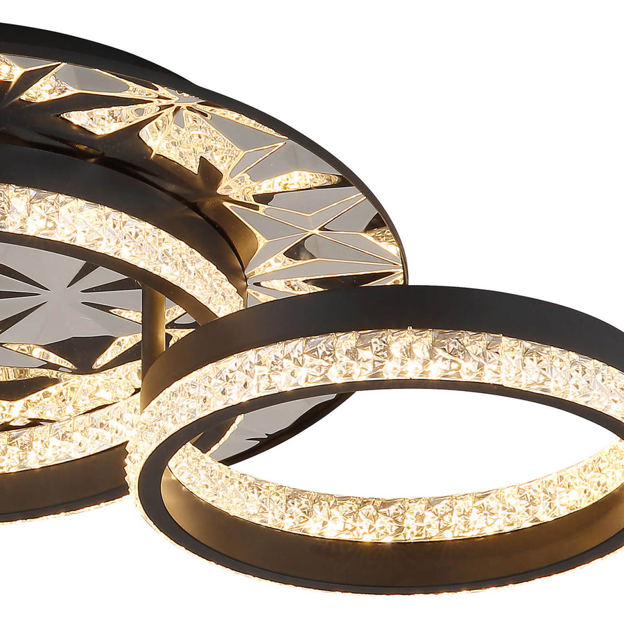Gros plan sur la bague en cristal illuminée et la structure métallique noire du luminaire.