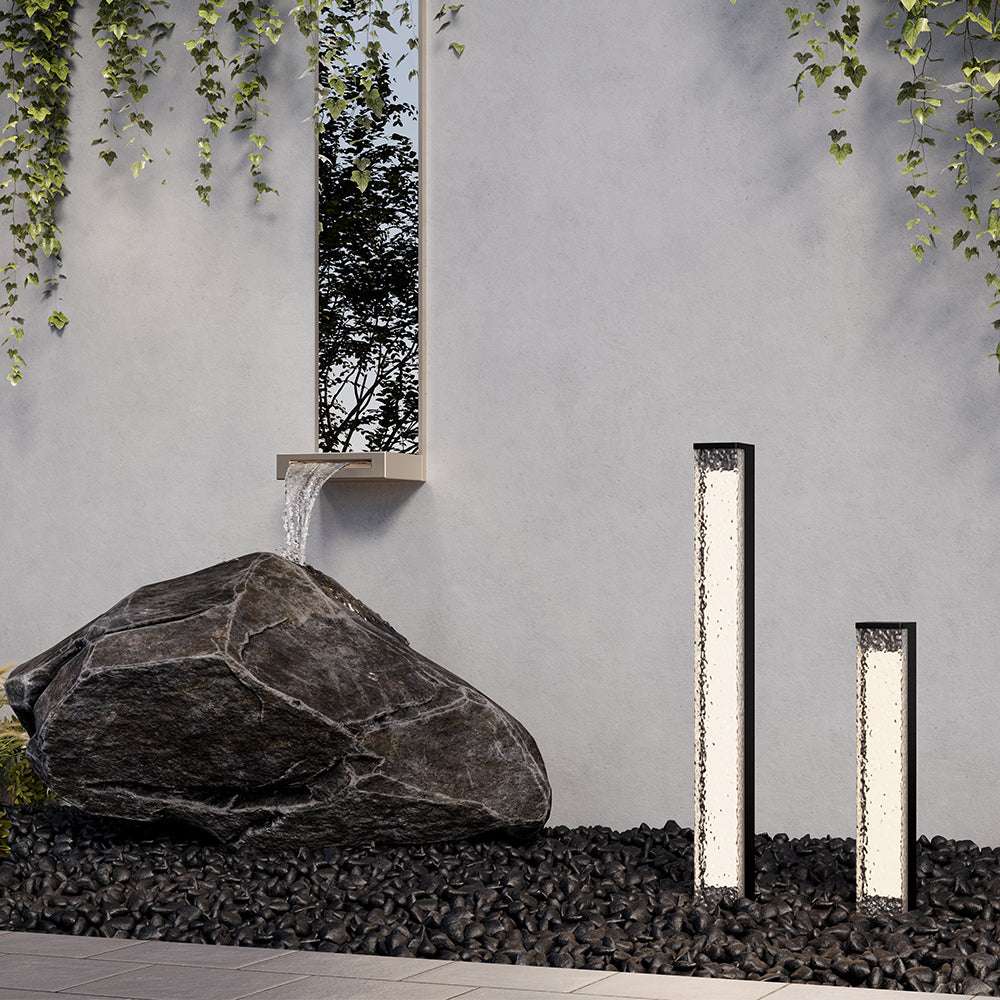 Mise en ambiance extérieure avec deux bornes lumineuses de hauteurs différentes près d'un rocher