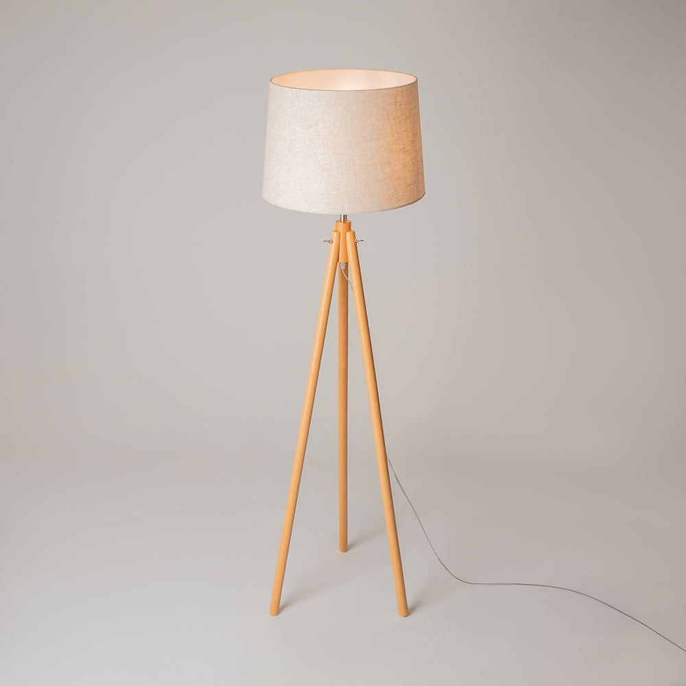 Lampadaire sur pied en bois clair, abat-jour beige et câble électrique au sol.