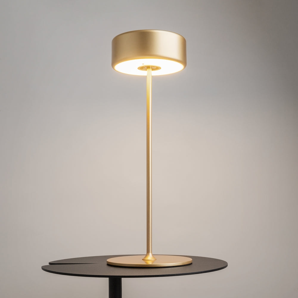 Lampe dorée allumée posée sur table noire, éclairage chaud diffusé vers le bas.