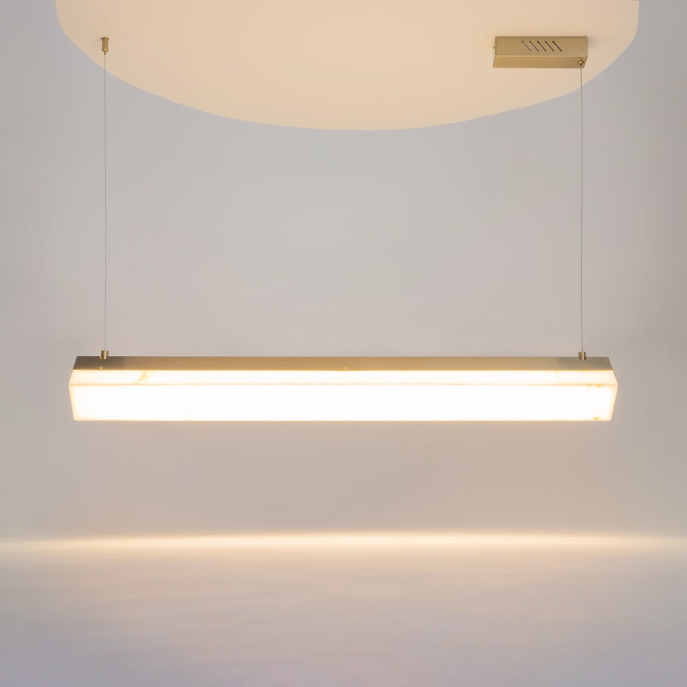 Luminaire suspendu allumé, longue barre lumineuse et câbles devant plafond clair.