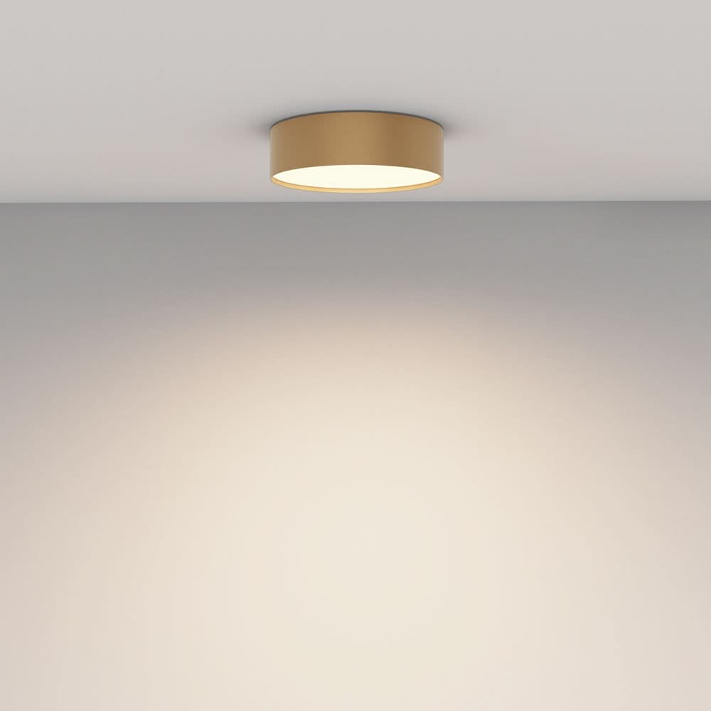 Luminaire doré fixé au plafond blanc, halo de lumière chaude diffusée sur le mur.
