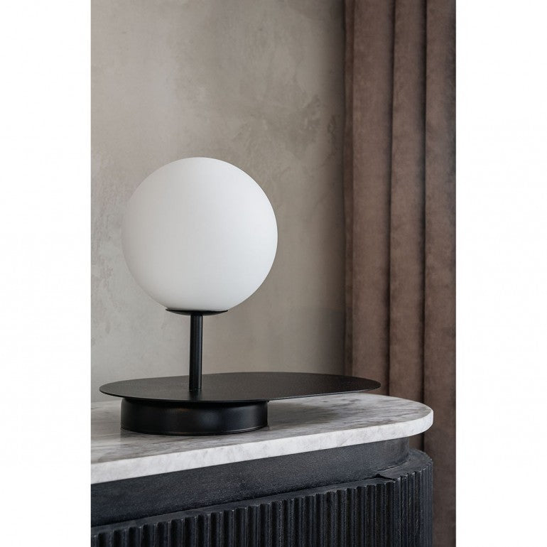 Lampe noire posée sur une table en marbre devant un mur beige et un rideau