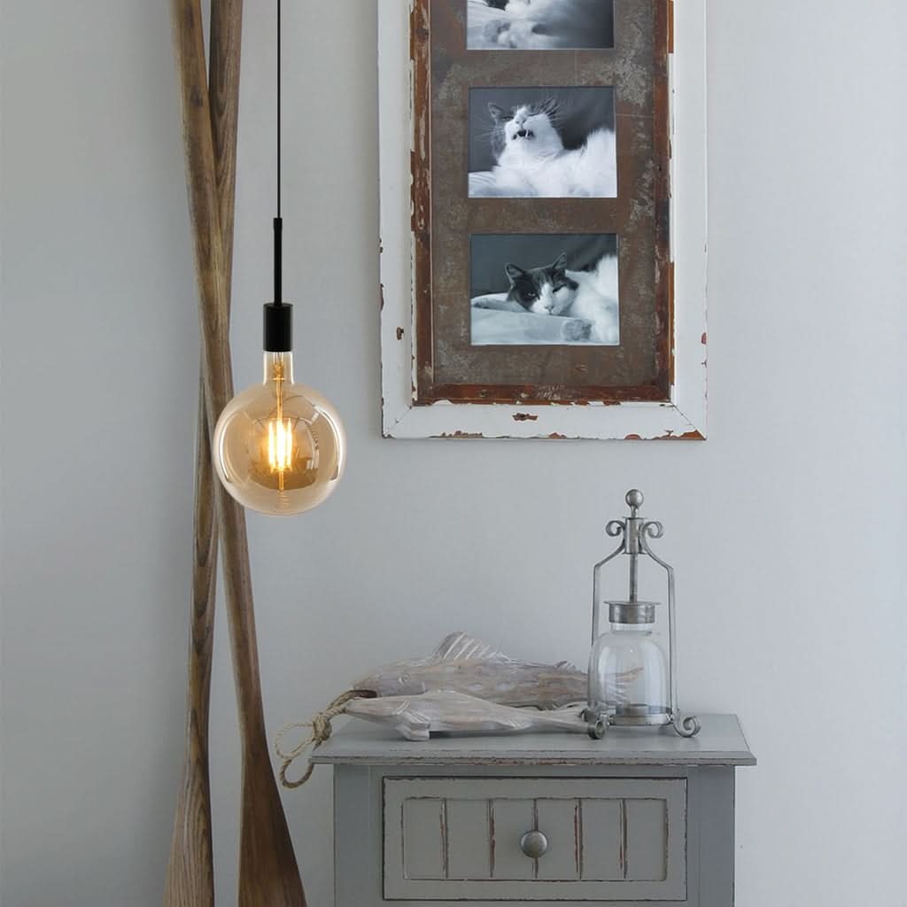Mise en ambiance de la suspension noire allumée dans un intérieur décoré avec meuble et cadres.