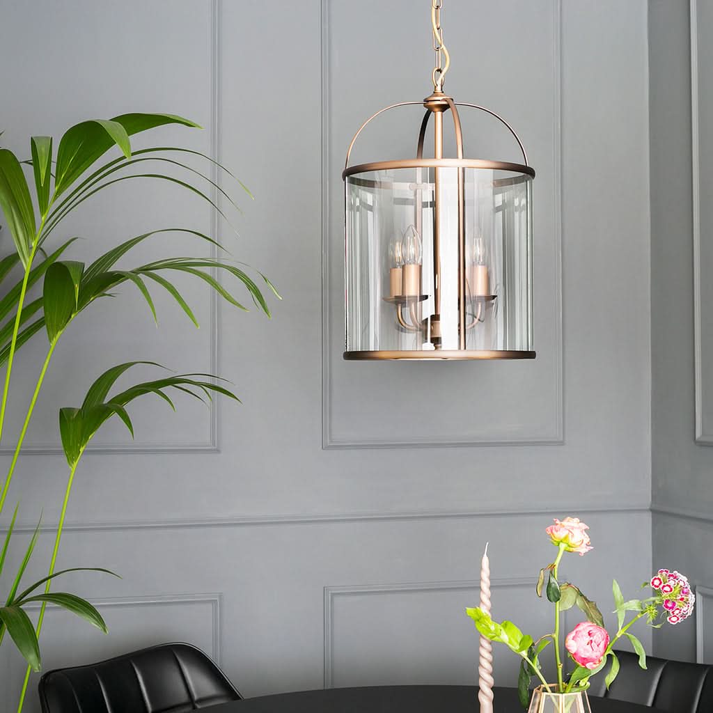 Suspension lanterne bronze suspendue au-dessus d'une table, cage en verre clair dans un intérieur gris