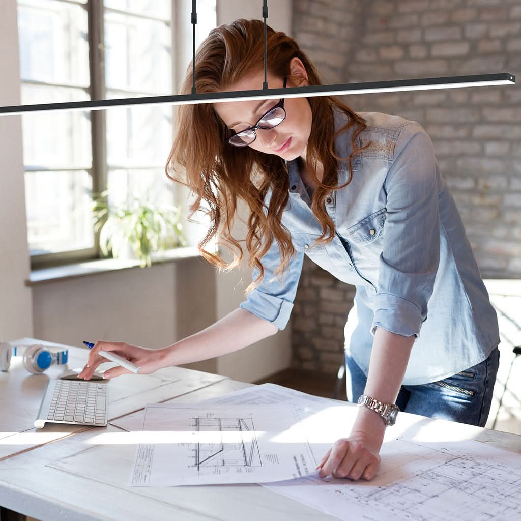 Mise en ambiance avec femme dessinant sur un bureau, suspension linéaire noire au-dessus.