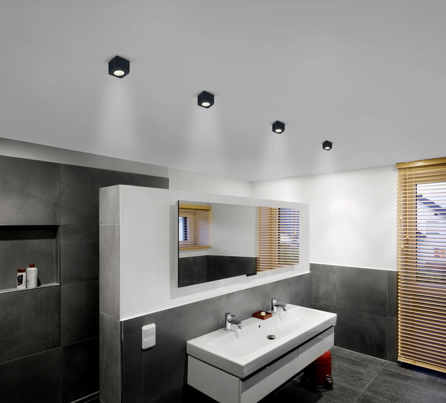 Vue d'ensemble d'une salle de bain avec quatre plafonniers noirs carrés fixés au plafond.