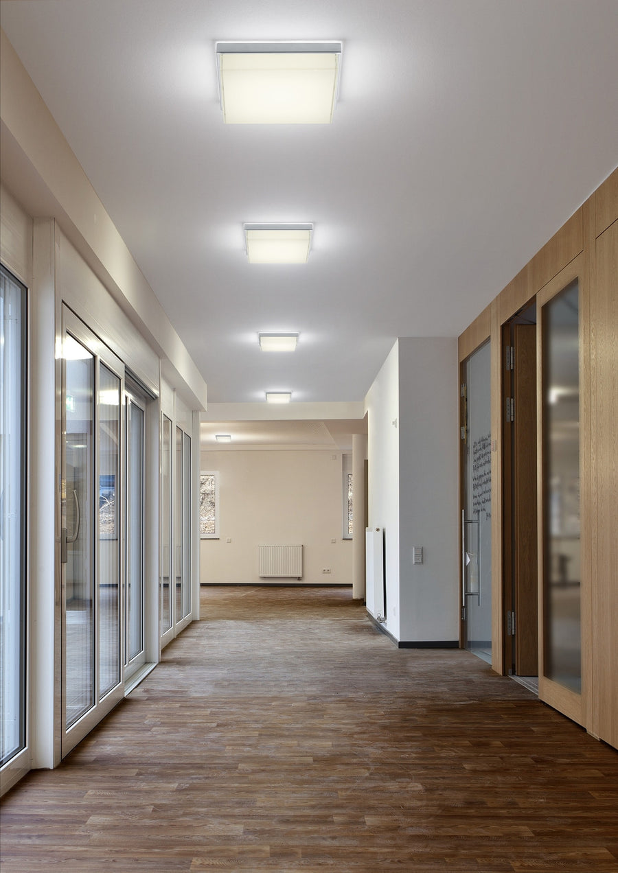 Mise en ambiance : alignement de plafonniers carrés éclairant un long couloir de bureau.