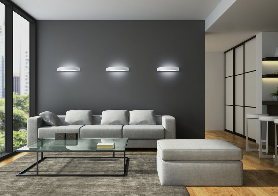 Trois appliques murales identiques éclairent un salon contemporain au-dessus d'un canapé gris.