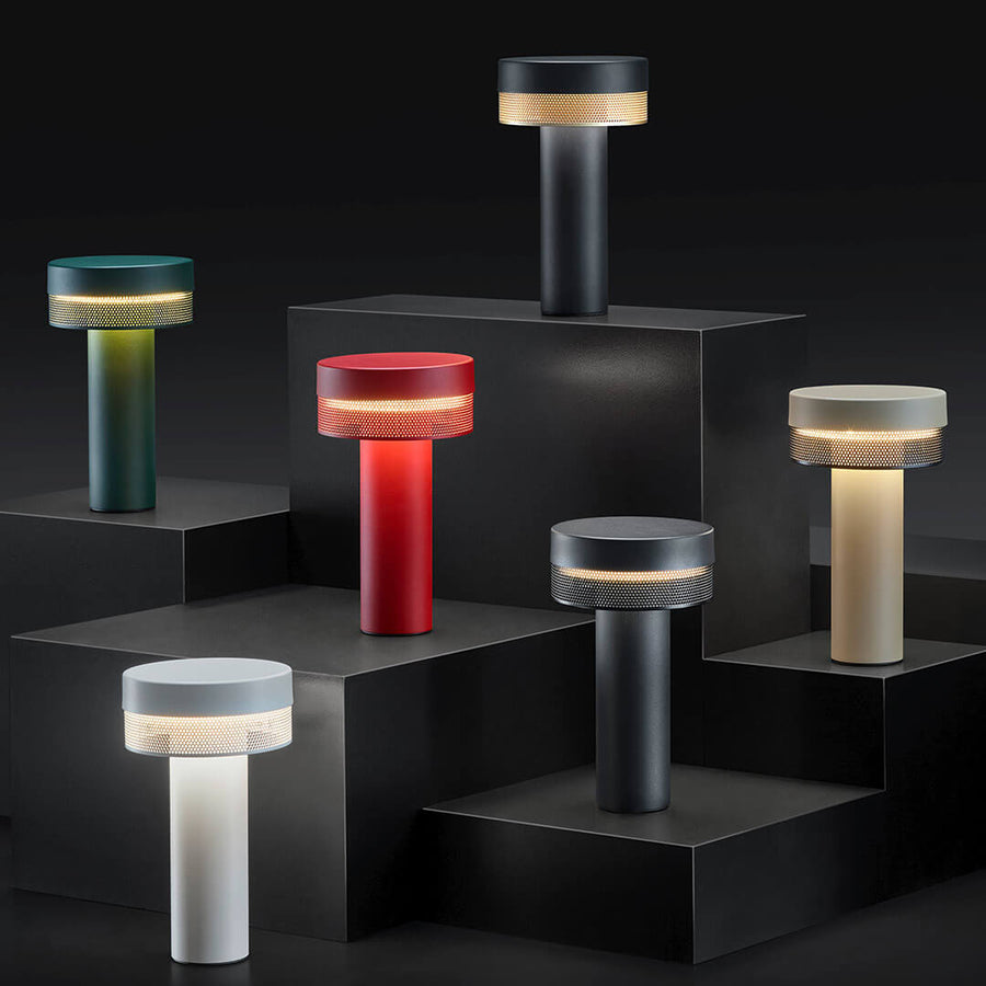 Plusieurs exemplaires colorés du luminaire posés sur des socles noirs en escalier.