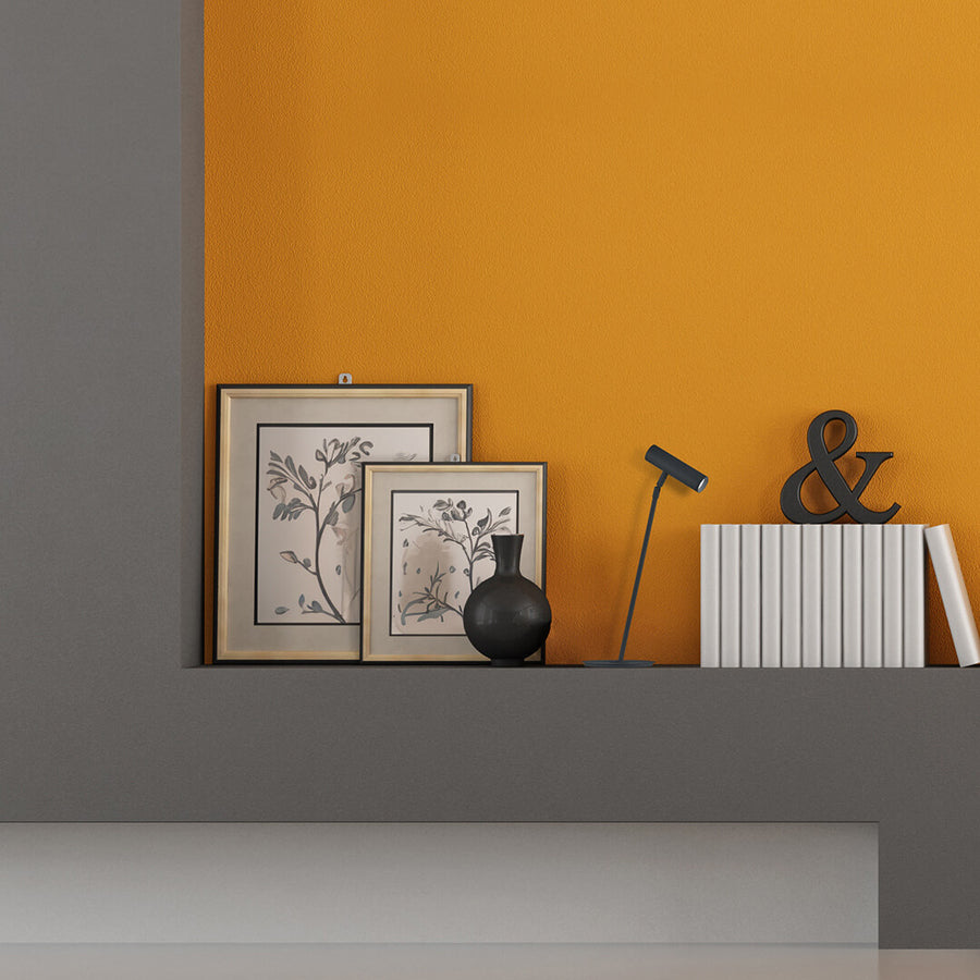 Lampe noire posée sur une étagère, cadres et livres devant mur orangé.