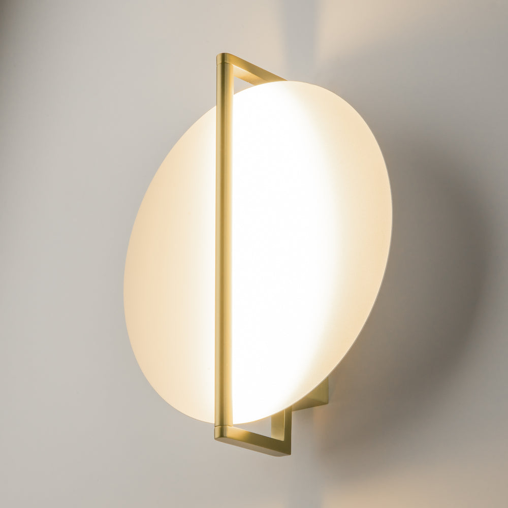 Vue de trois quarts allumée : cadre rectangulaire en laiton et diffuseur ovale lumineux fixé au mur.