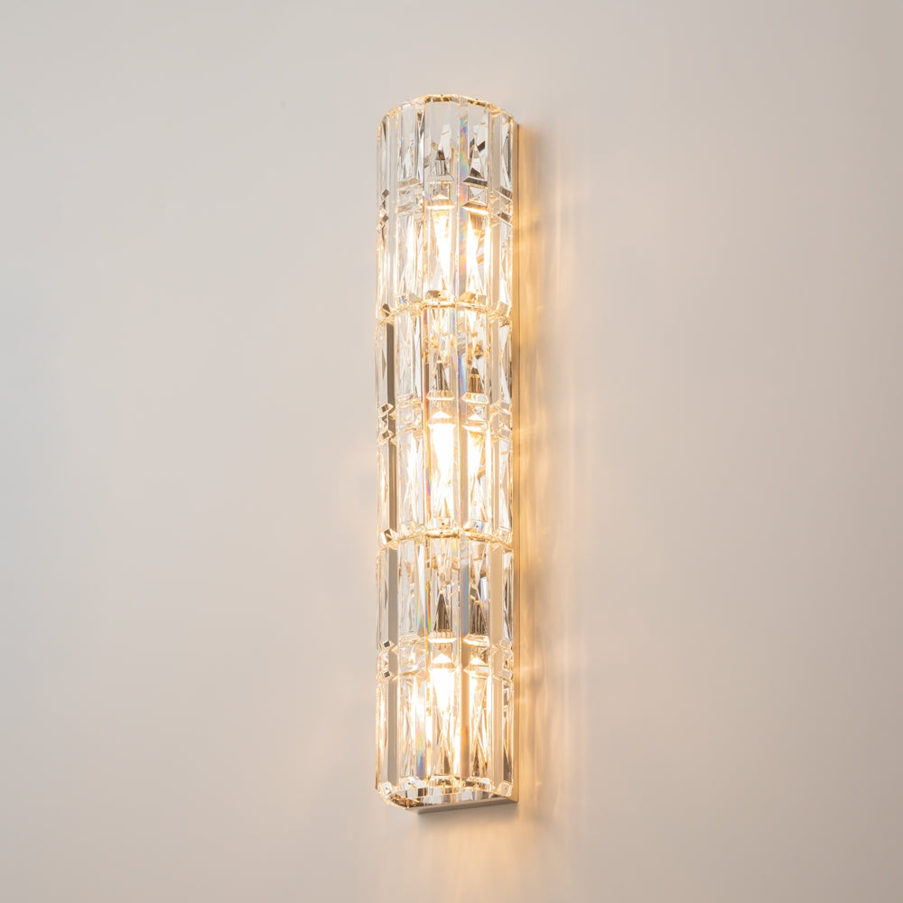 Applique allumée sur mur beige, halo doré et reflets du cristal taillé.