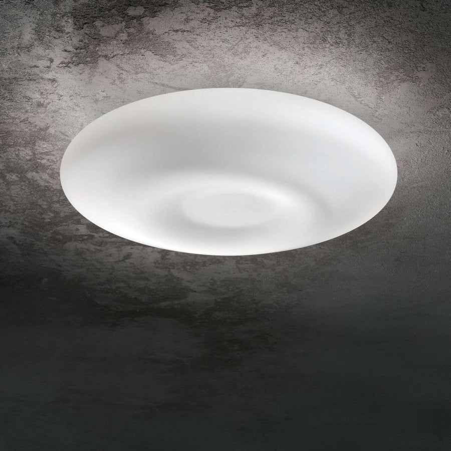Diffuseur blanc allumé fixé au plafond, halo lumineux sur béton gris texturé